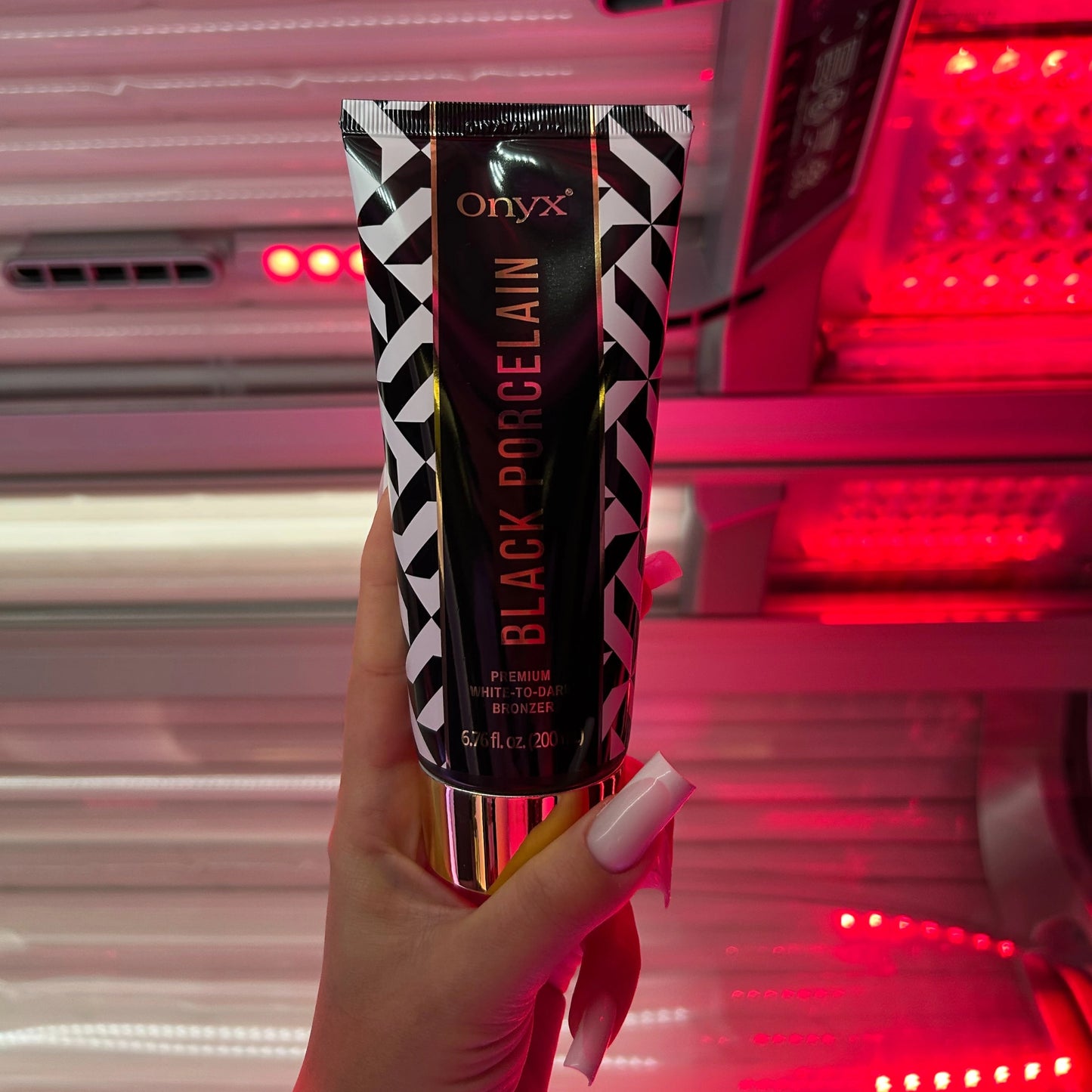 Hand hält Onyx Black Porcelain Bräunungslotion vor intensivem Rotlicht im Solarium, Produkt ideal für White-to-Dark Tanning