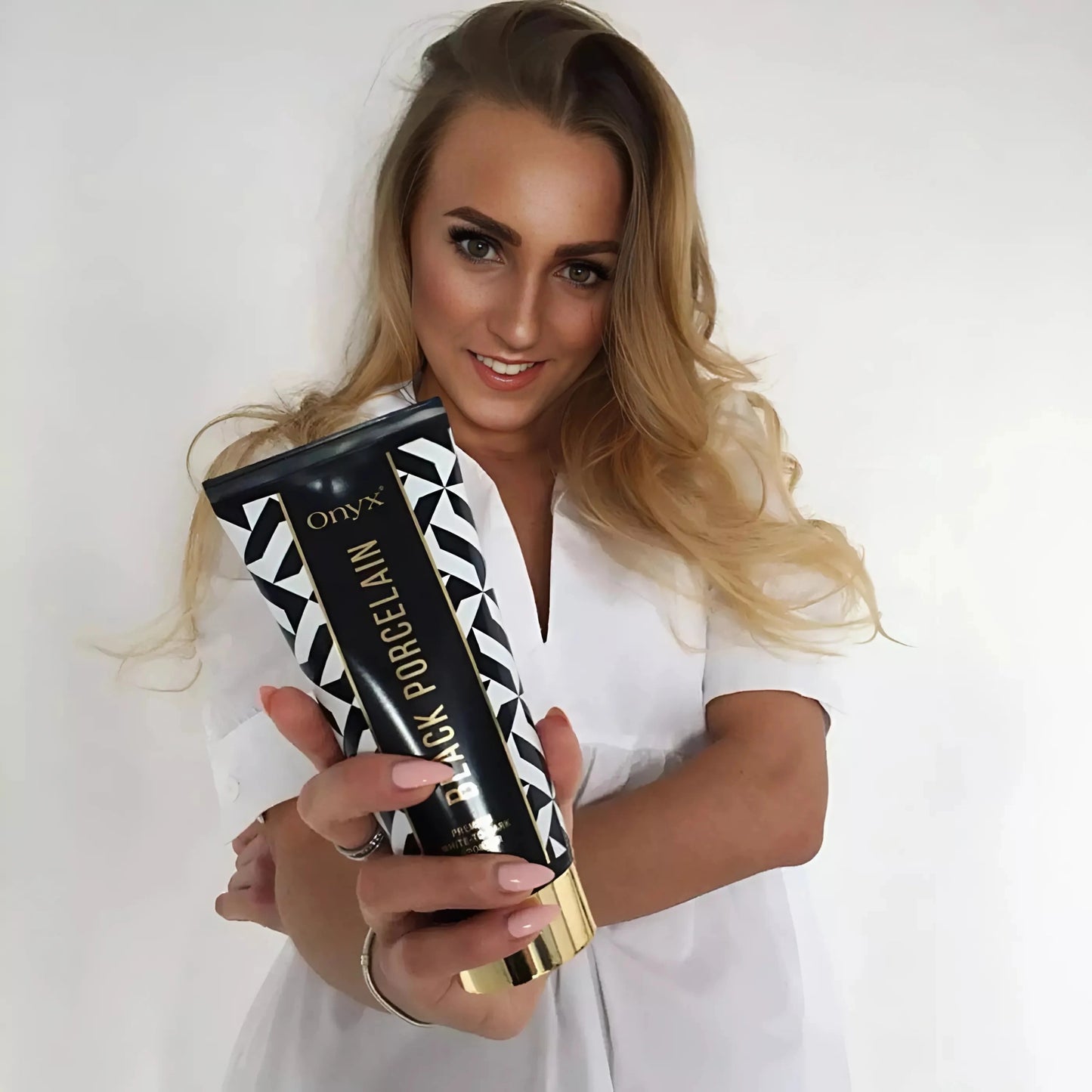 Nahaufnahme einer blonden Frau mit Onyx Black Porcelain Bräunungslotion, zeigt das Produkt mit einem freundlichen Lächeln
