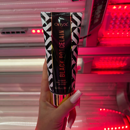 Hand hält Onyx Black Porcelain Bräunungslotion vor intensivem Rotlicht im Solarium, Produkt ideal für White-to-Dark Tanning