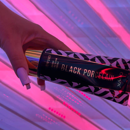 Onyx Black Porcelain Tanning Lotion liegt in einer Hand mit langen Nägeln vor pinkem Licht im Solarium